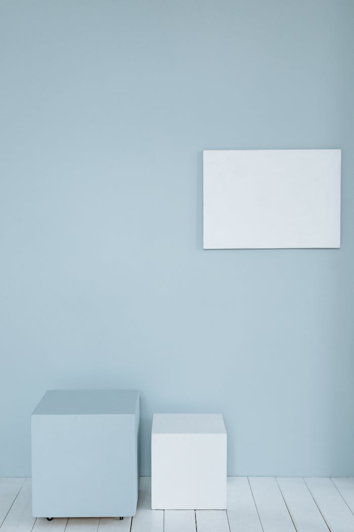 A minimalist room with a blank canvas on a pastel wall and two cubes for mockup design.
